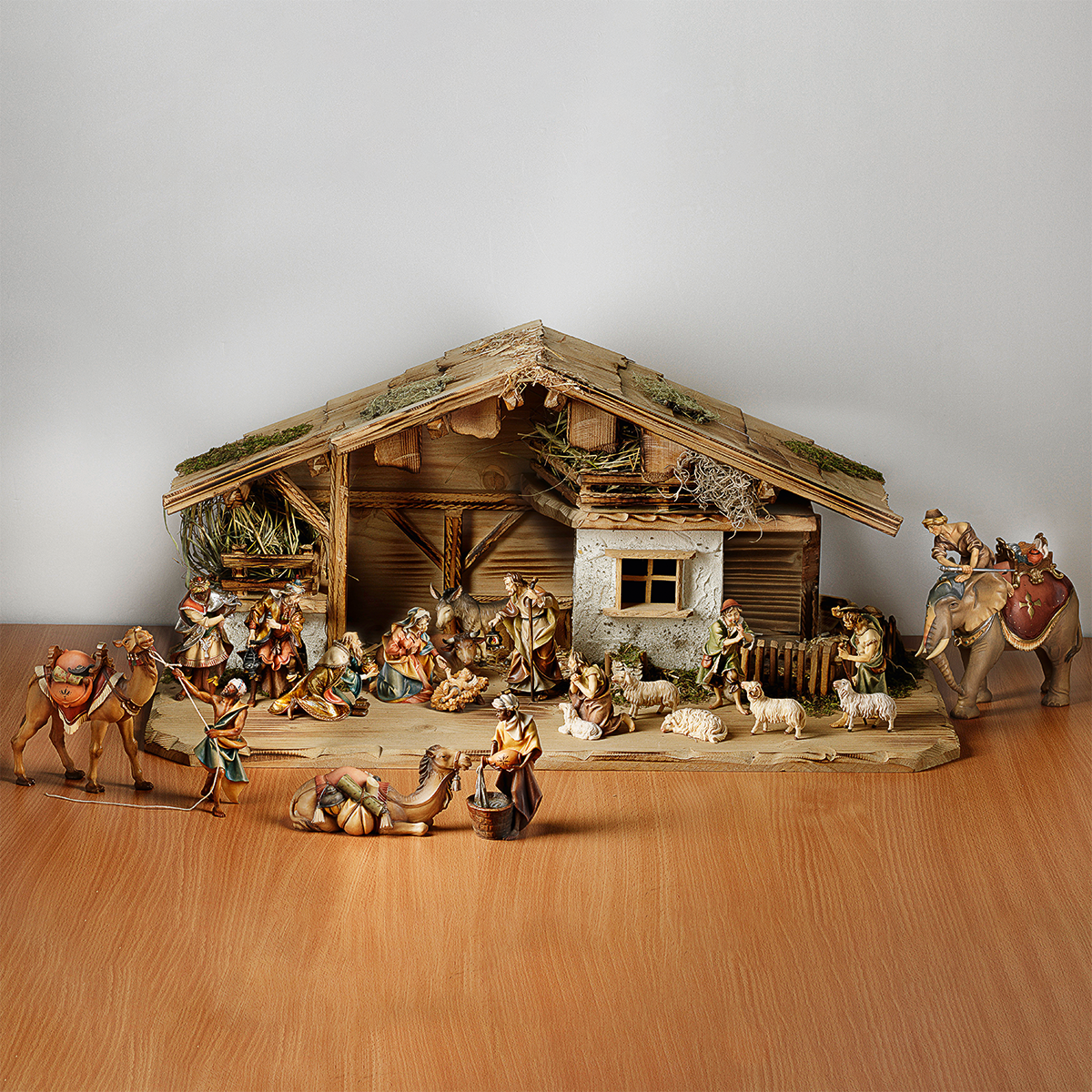 Handgeschnitzte Krippe aus Holz mit 20 detailreichen Figuren, darunter die Heilige Familie, die Heiligen Drei Könige, Hirten, verschiedene Tiere und ein Stall. Die Szene ist traditionell gestaltet und eignet sich als festliche Weihnachtsdekoration auf einer Holzoberfläche.