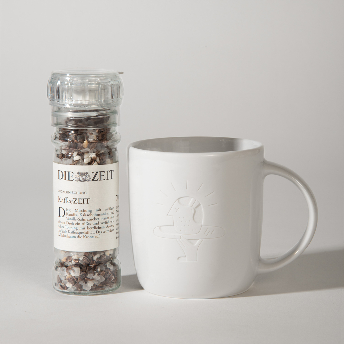 Ein Geschenkset bestehend aus einer weißen Tasse mit einem geprägten Vogelmotiv und einer Gewürzmischung von 'Die Zeit' mit dem Etikett 'KaffeeZEIT'.