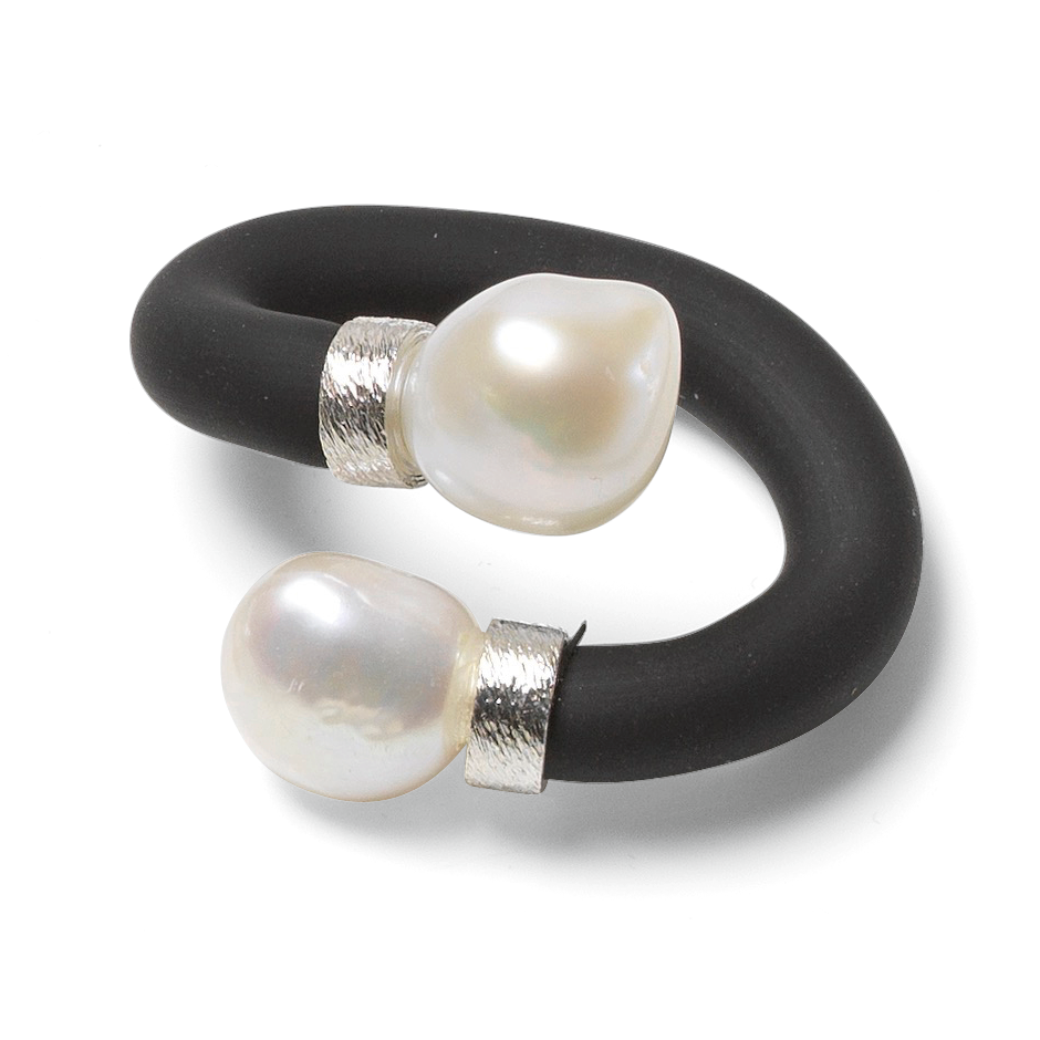 Der abgebildete Ring aus dem Schmuckset "Mother of Pearl" von Ars mundi zeigt ein modernes Design mit einem offenen, schwarzen Ringband aus Kautschuk und zwei weißen, unregelmäßig geformten Perlen an den Enden. Die Enden sind mit silbernen Elementen eingefasst.