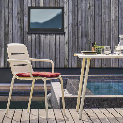 Zwei bequeme Sessel »VAPIO« und ein runder Tisch auf einer Holzterrasse am Pool vor einem modernen Gebäude.