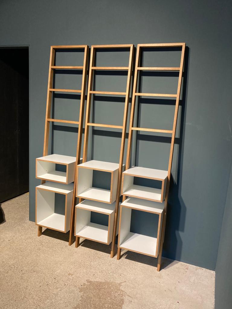 Drei Leitregale aus hellem Holz mit weißen Fächern, die vor einer dunkelgrauen Wand stehen.