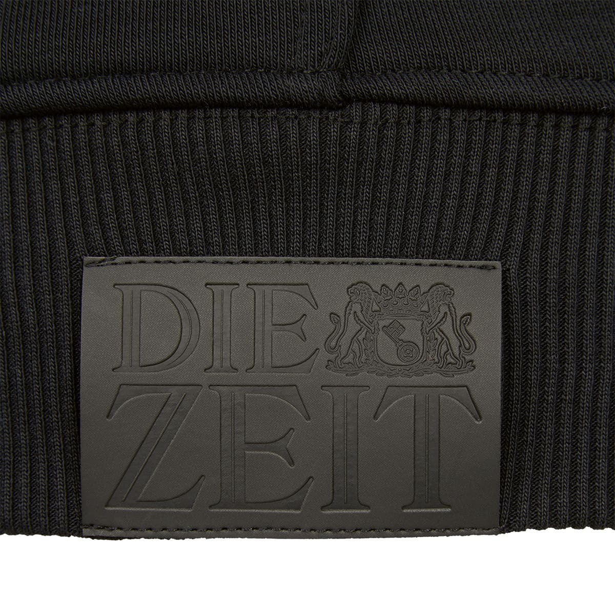 Nahaufnahme eines schwarzen Hoodies der ZEIT-Kollektion mit einem eingeprägten 'DIE ZEIT' Logo und zwei stilisierten Löwen.