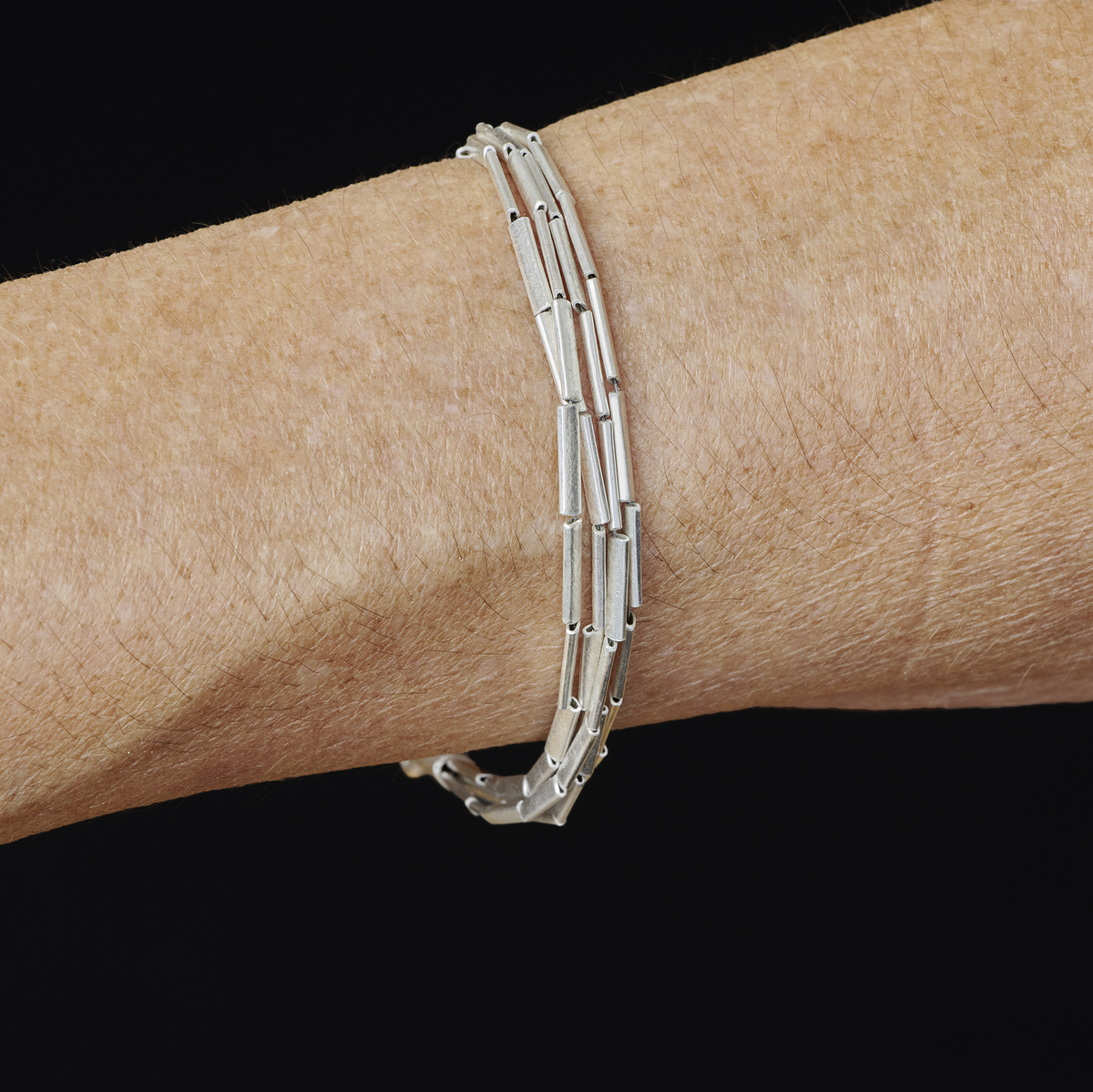 Silbernes Armband in Halm-Optik am Handgelenk einer Person, auf schwarzem Hintergrund. Das elegante Schmuckstück wirkt modern und dezent.