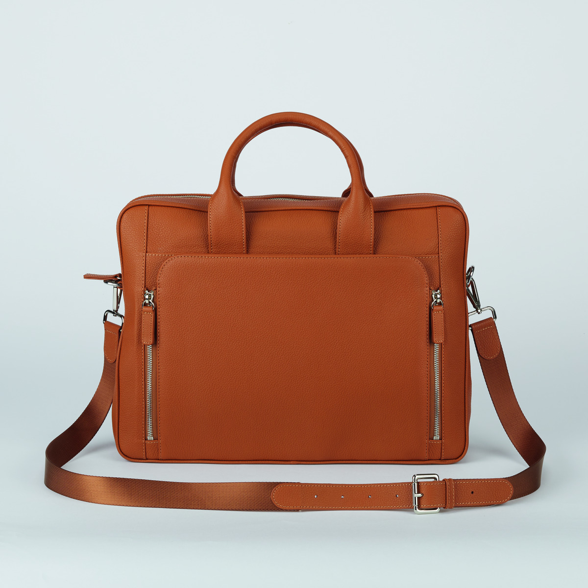 Eine braune Business-Tasche aus Leder mit einem Schultergurt und zwei Reißverschlussfächern auf der Vorderseite. Die Tasche verfügt über zwei Tragegriffe.