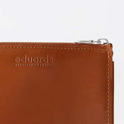 Detailansicht einer braunen Lederbrieftasche »Näver« der Marke Eduards Accessories AB mit sichtbarem Reißverschluss und Logo-Prägung auf der glatten Oberfläche. Hochwertig verarbeitet, zeitlos, ideal für Karten und Kleinigkeiten.