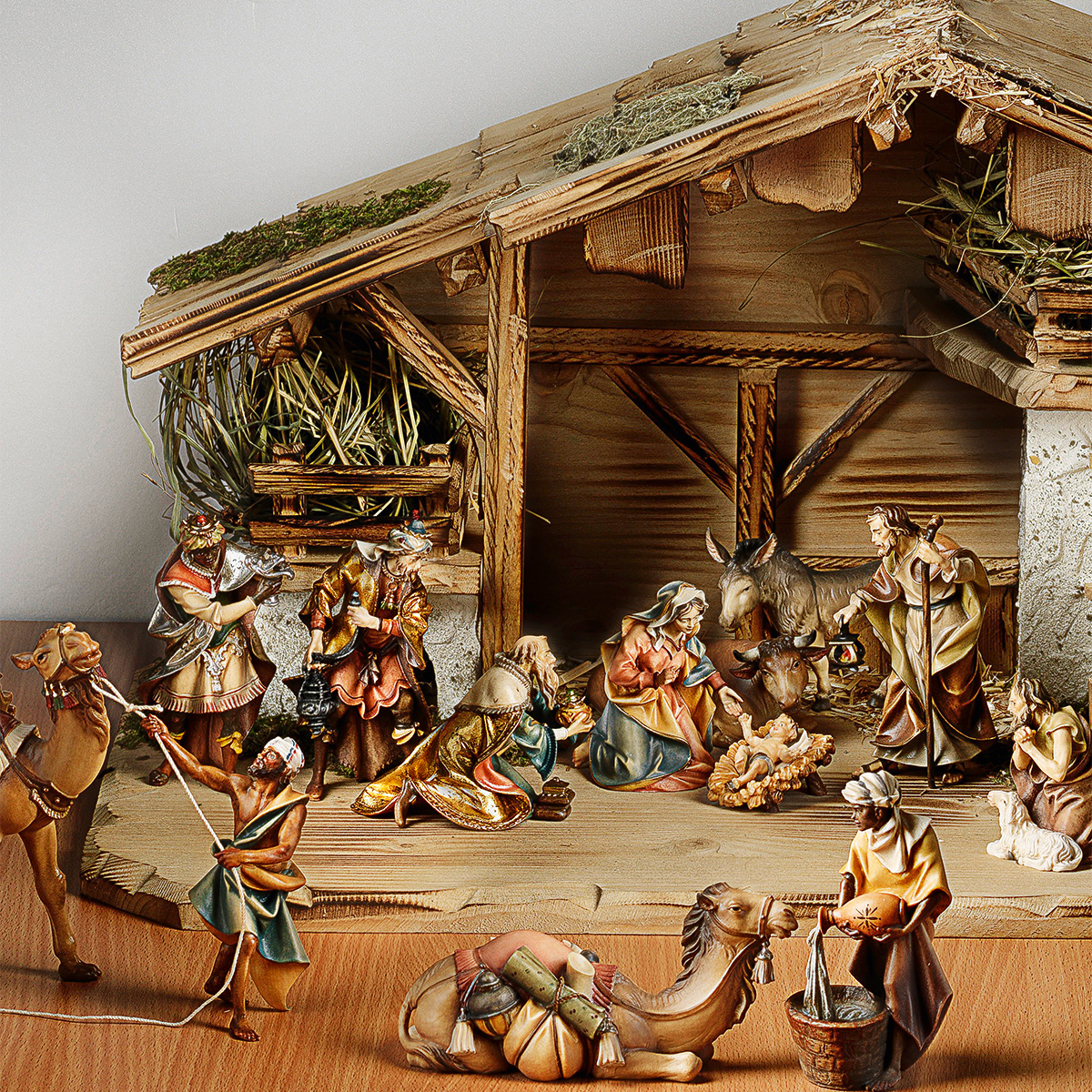 Handgeschnitzte 20-teilige Holzkrippe zeigt eine detaillierte Weihnachtskrippenszene mit Heilige Familie, Tieren, Hirten und den Heiligen Drei Königen in einem offenen Stall mit Stroh und rustikalem Dach. Die Figuren sind liebevoll gestaltet und in warmen Naturfarben bemalt.
