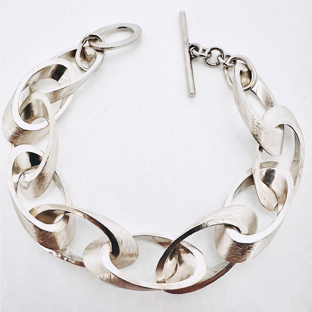 Silbernes Kettenarmband mit großen, flachgedrückten Gliedern und einem T-Verschluss, auf weißem Hintergrund dargestellt.