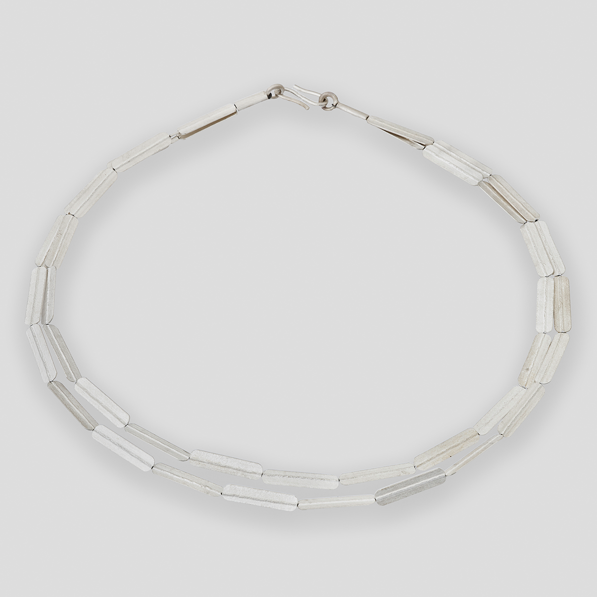 Silbernes Collier mit geprägten, länglichen Stabelementen, die abwechselnd angeordnet sind. Die Halskette wirkt modern und minimalistisch, besonders geeignet als eleganter Halsschmuck für verschiedene festliche Anlässe oder als stilvolles Accessoire im Alltag.