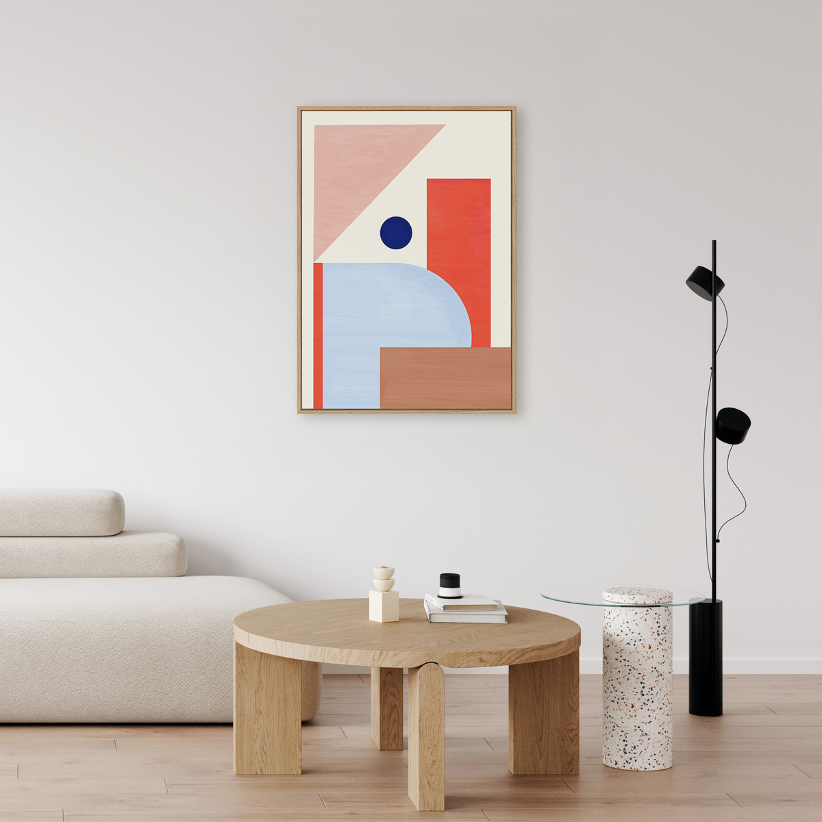 Abstraktes Leinwandbild in geometrischem Stil an einer weißen Wand über einem minimalistischen beigen Sofa und einem runden Holztisch, mit modernen Dekorationselementen in einem hell eingerichteten Wohnzimmer.
