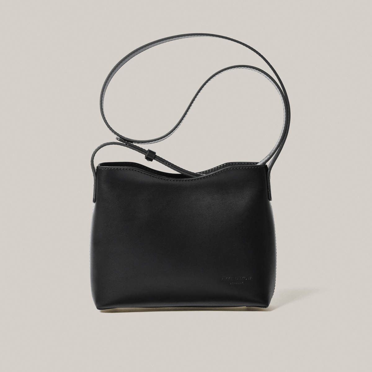 Schwarze Schultertasche aus Kernleder vor einem hellgrauen Hintergrund.