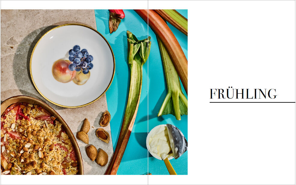 Kochbuch »Frisch vom Wochenmarkt« mit einer Illustration zum Thema Frühling. Abgebildet sind frische Lebensmittel wie Rhabarber, Beeren und Nüsse sowie verschiedene Gerichte in Tellern auf einem hellen Hintergrund.