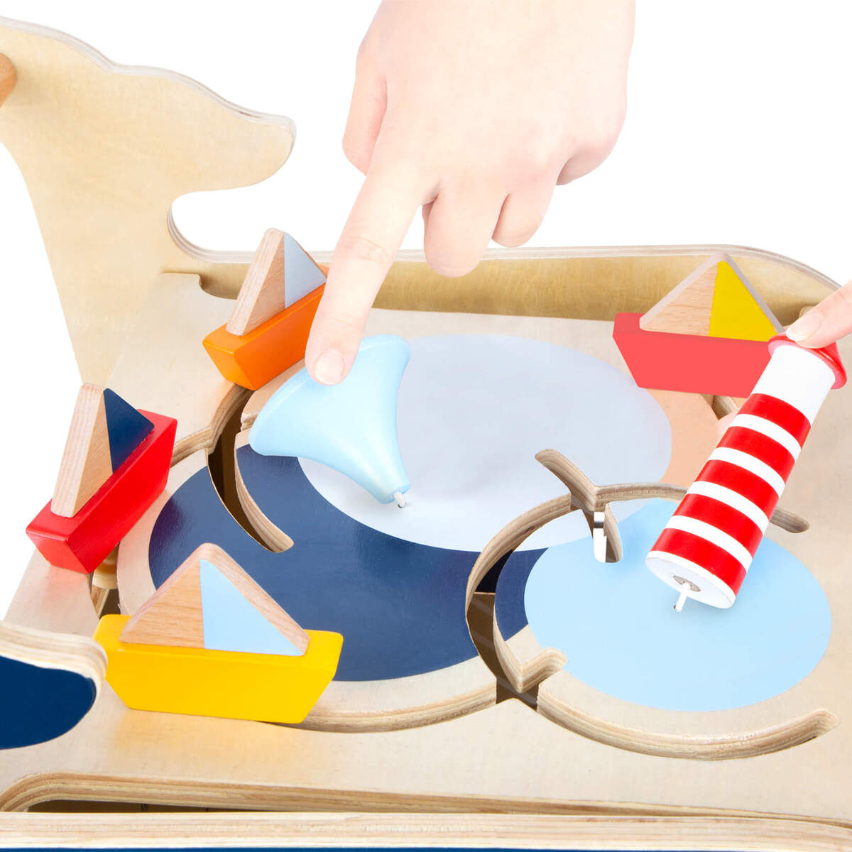 Abgebildet ist ein Lauflernwagen in Form eines Wals aus Holz. Der Wagen hat ein maritimes Design mit kleinen, bunten Holzbooten und einer dreifarbigen, gestreiften Spielfigur. Zwei Kinderhände sind im Bild zu sehen, die mit den Spielteilen interagieren. Das Spielzeug fördert die Motorik und das Lernen bei Kleinkindern.
