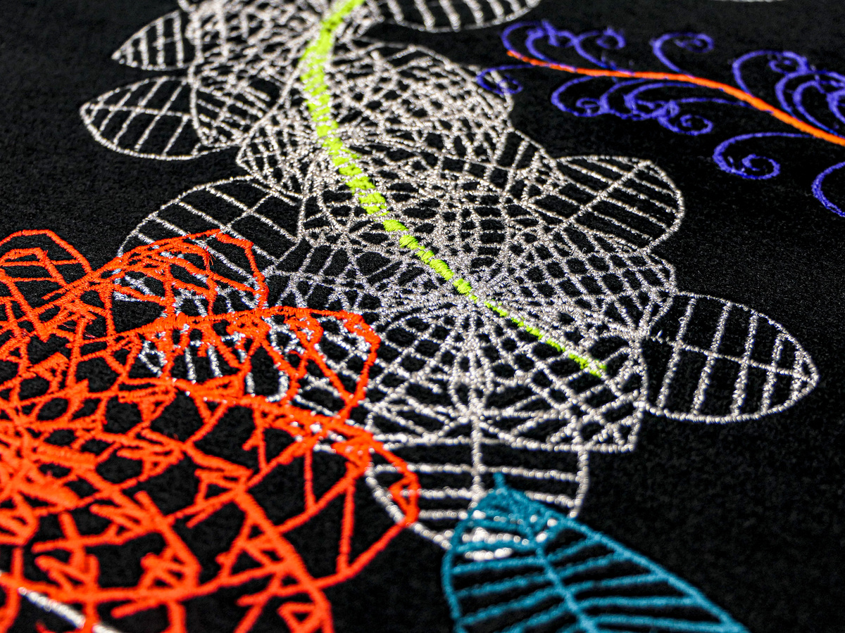 Detailreiche Nahaufnahme einer bestickten Textil-Edition von Miguel Chevalier, 2024, aus der ZEIT Sonderedition »Extra-Natural«. Die Stickerei zeigt abstrakte, farbenfrohe Muster in Rot, Blau, Grün, Weiß und Lila auf schwarzem Hintergrund.