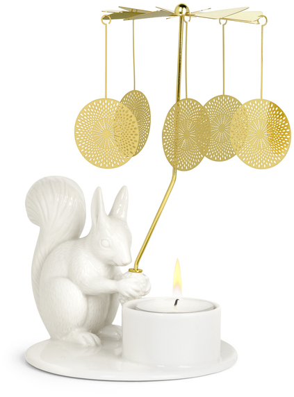 Ein weißes Eichhörnchen aus Keramik hält ein Engelsglockenspiel, das über einem Teelicht steht. Die flachen, runden Anhänger des Spiels sind golden und reflektieren das Licht der Kerze.