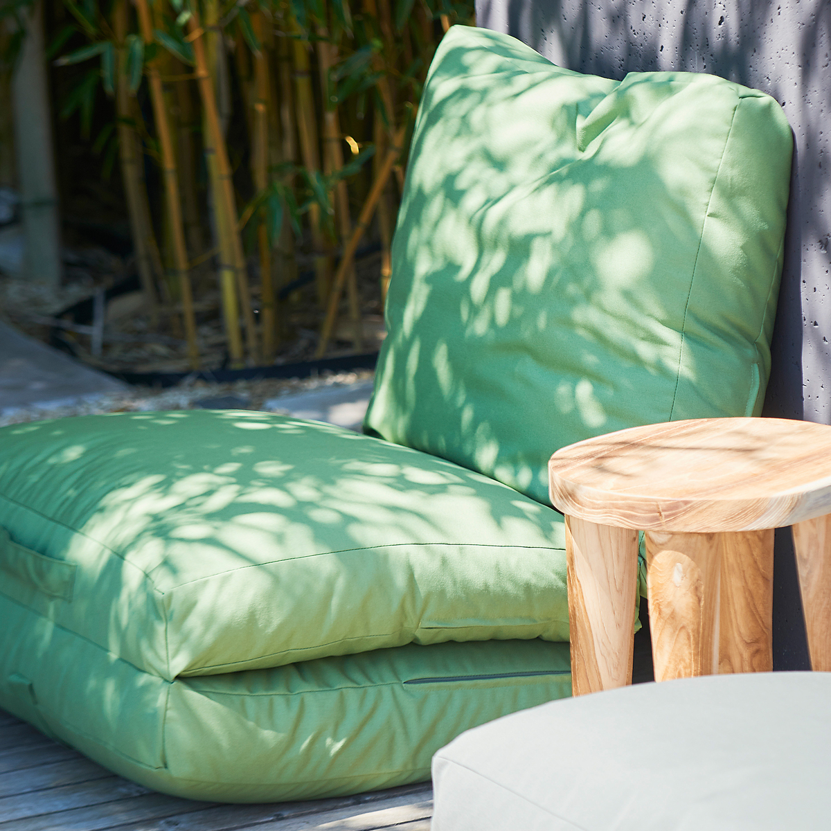 Eine grüne Gartenmatratze »Sheffield« mit Rückenstütze neben einem kleinen Holztisch auf einer Terrasse mit Bambus im Hintergrund.