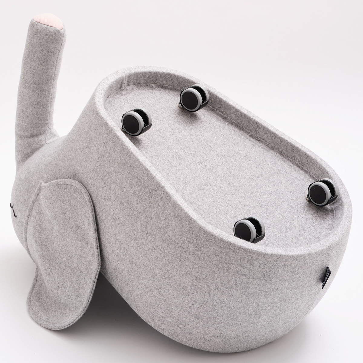 Ein Rollelefant namens »bou« mit einem weichen, grauen Stoffbezug und Holzrollen. Das Produkt, ein Kinderspielzeug und Sitzhocker in Elefantenform, ist auf einem weißen Hintergrund abgebildet.