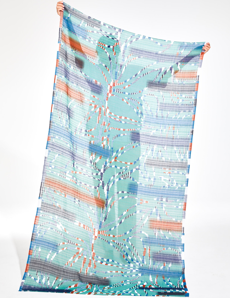 Ein Baumwolltuch mit dem Namen 'Ivy', das ein farbenfrohes Muster aus Blau-, Grün-, Orange-, Weiß- und Rosatönen aufweist. Das Tuch hängt von oben herunter und zeigt ein einzigartiges Design, das als modisches Accessoire oder Dekorationsstück verwendet werden kann.