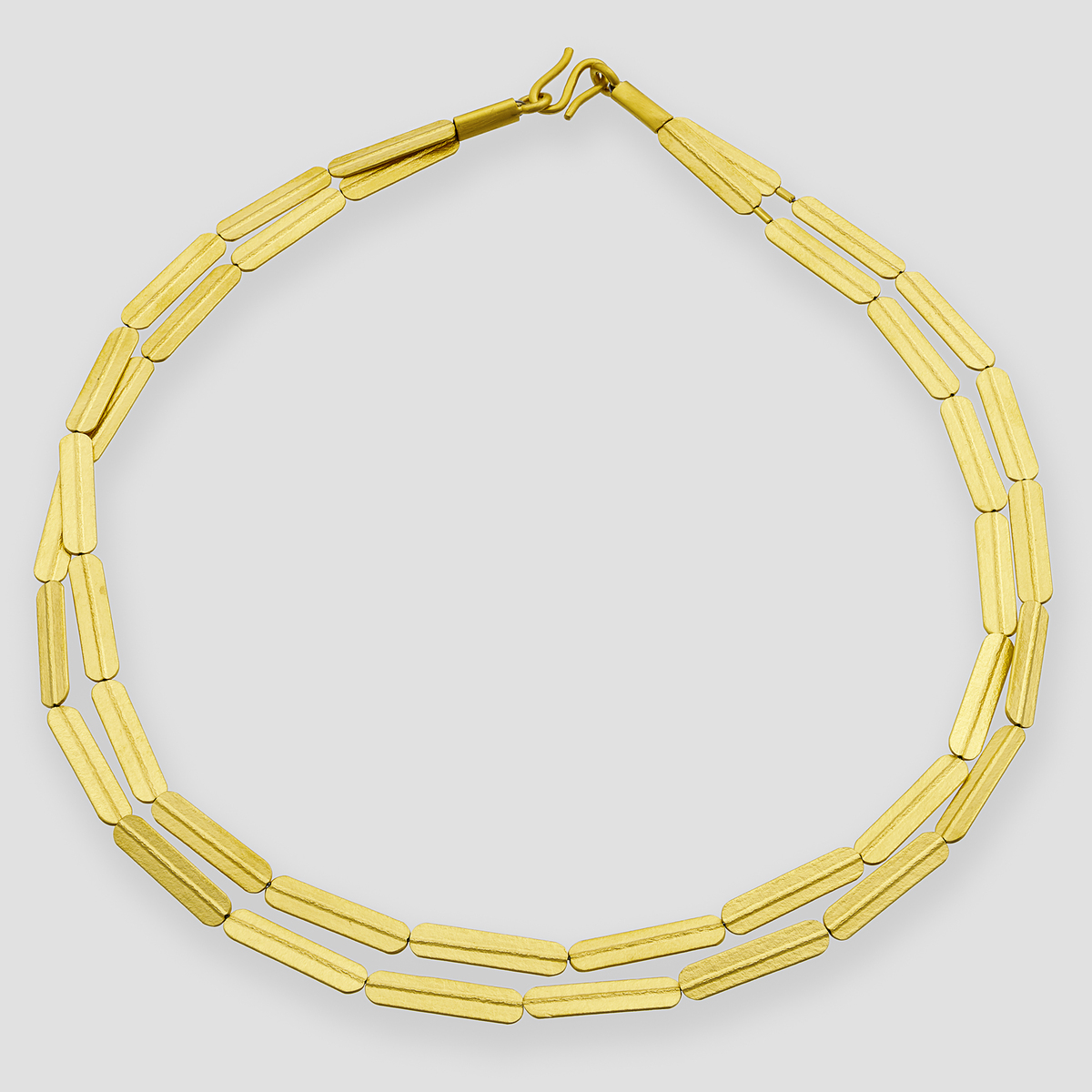 Goldfarbenes und silberfarbenes Collier mit gestreifter, länglicher Gliederstruktur, aus Silber gefertigt und feingoldplattiert. Das moderne Design liegt flach auf grauem Hintergrund und zeigt die hochwertige Verarbeitung des Schmuckstücks, geeignet als elegantes Accessoire für verschiedene Anlässe.