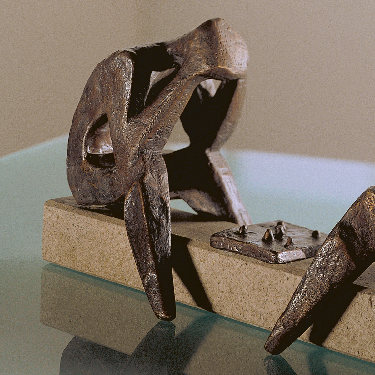 Detailreiche Bronzeskulptur von Sepp Mastaller: Zwei abstrahierte Figuren sitzen an einem rechteckigen Steintisch mit Schachbrett, ausgeführt im Wachsausschmelzverfahren. Oberfläche matt glänzend, feine Konturen. Die Skulptur steht auf einem massiven Sockel aus hellem Stein.