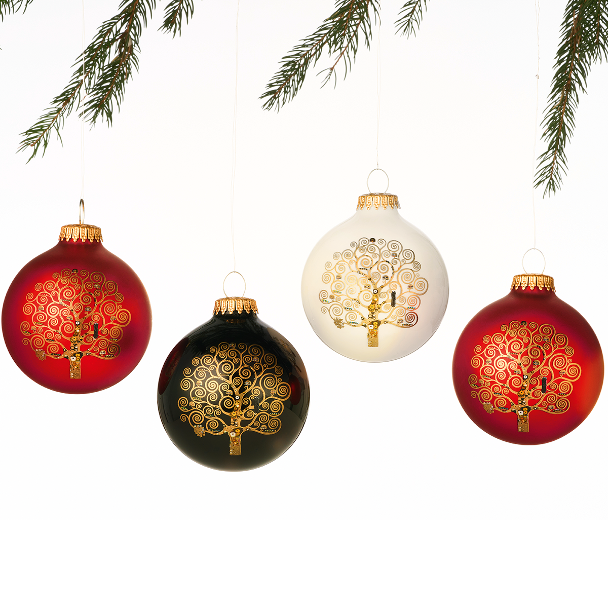 Vier edle Weihnachtsbaumkugeln aus Glas im Set mit dem Lebensbaum-Motiv nach Gustav Klimt, drei davon in Rot und eine in Weiß, jeweils mit goldener Verzierung. Die Kugeln hängen an goldenen Aufhängern und sind vor weißem Hintergrund mit einigen grünen Tannenzweigen dekorativ arrangiert.