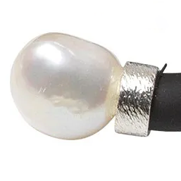 Nahaufnahme eines Rings aus dem Schmuckset "Mother of Pearl" von Ars mundi. Der Ring besteht aus einer großen, weißen Perle und einer breiten, strukturierten Fassung aus 925er-Sterlingsilber, die auf ein schwarzes Band aufgezogen ist. Hochwertige Materialien und eleganter Look.