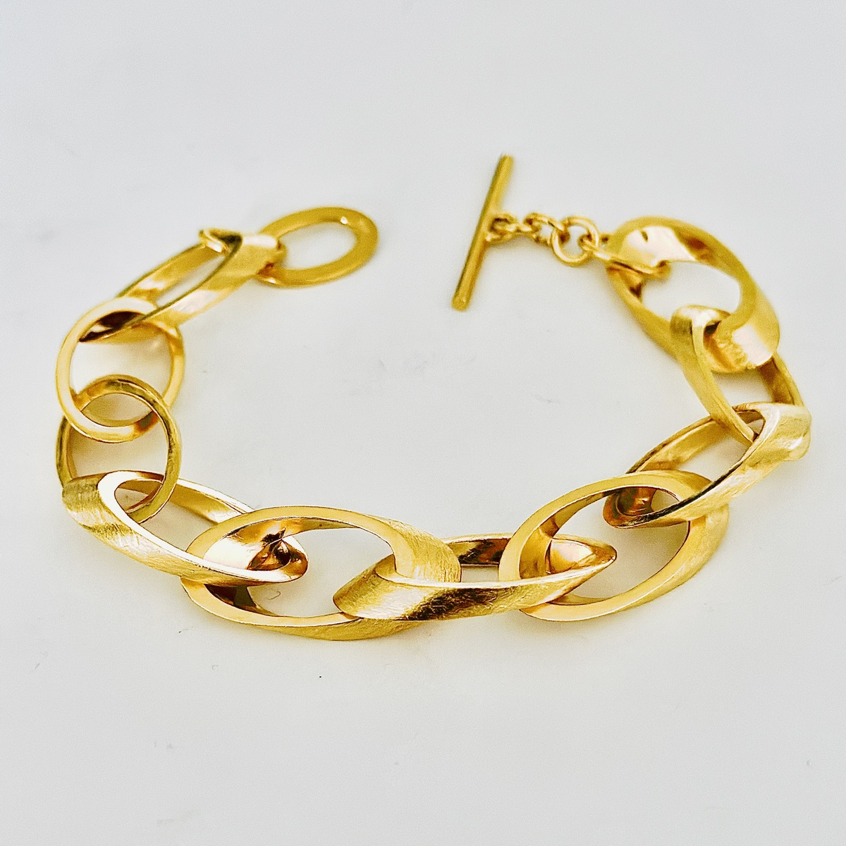 Ein feingoldplattiertes Silberarmband mit stilvollen Kettengliedern vor weißem Hintergrund.
