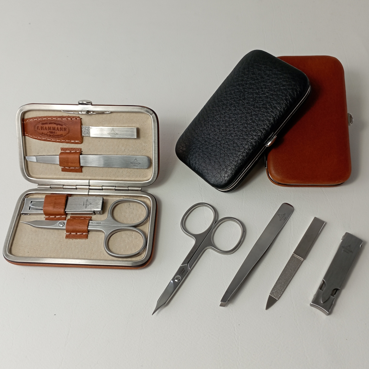 Ein Maniküre-Set besteht aus verschiedenen Werkzeugen zur Nagelpflege, wie Schere, Feile, Pinzette und Nagelknipser, ordentlich in einem schwarzen und braunen Lederetui arrangiert.