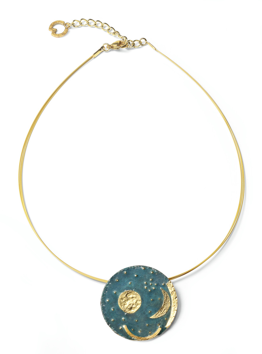 Das Bild zeigt das Petra Waszak Collier "Himmelsscheibe von Nebra". Mehrsträngig angeordnet, kombinieren die Ketten golden glänzende Metallelemente, türkisfarbene und grüne Perlen sowie eine runde, gold-schwarz-grün gemusterte Scheibe als zentrales Schmuckelement. Feine Lichtreflexe betonen die edlen Materialien.