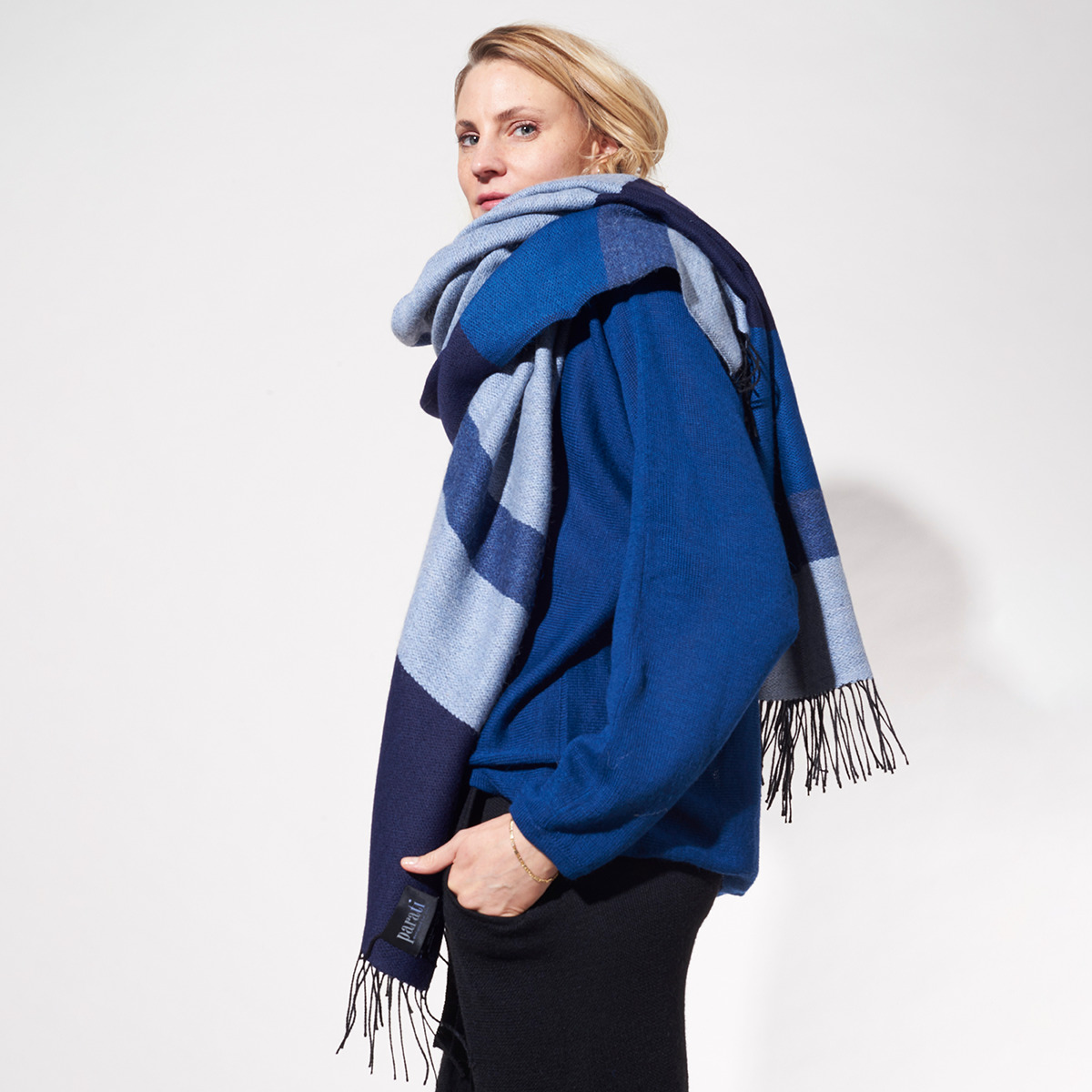 Eine Frau trägt ein blaues Cape aus der ZEIT-Jubiläumsedition »Shades of Blue«. Das Cape ist in verschiedenen Blautönen gestreift und hat Fransen an den Enden.