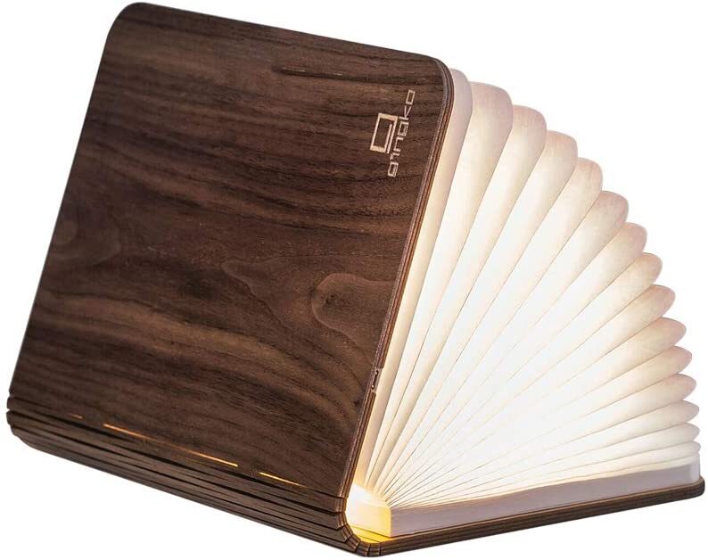 Eine zusammenklappbare LED-Buchlampe in Walnuss-Holzoptik. Das Licht scheint durch die weißen, aufgefächerten Buchseiten und strahlt ein warmes, gemütliches Licht aus. Perfekt als stilvolle Nachttischlampe oder dekoratives Element in jedem Raum.