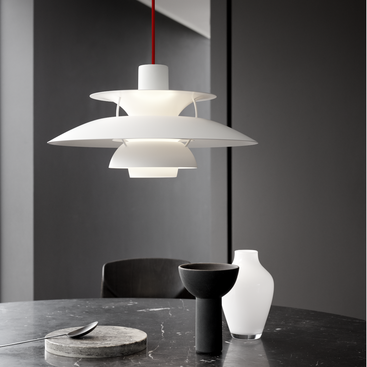 Moderne weiße Pendelleuchte der ZEIT-Sonderedition PH5 Monochrome mit rotem Kabel, stilvoll inszeniert über einem dunklen Marmortisch mit minimalistischen Dekorationen vor einer grauen Wand.