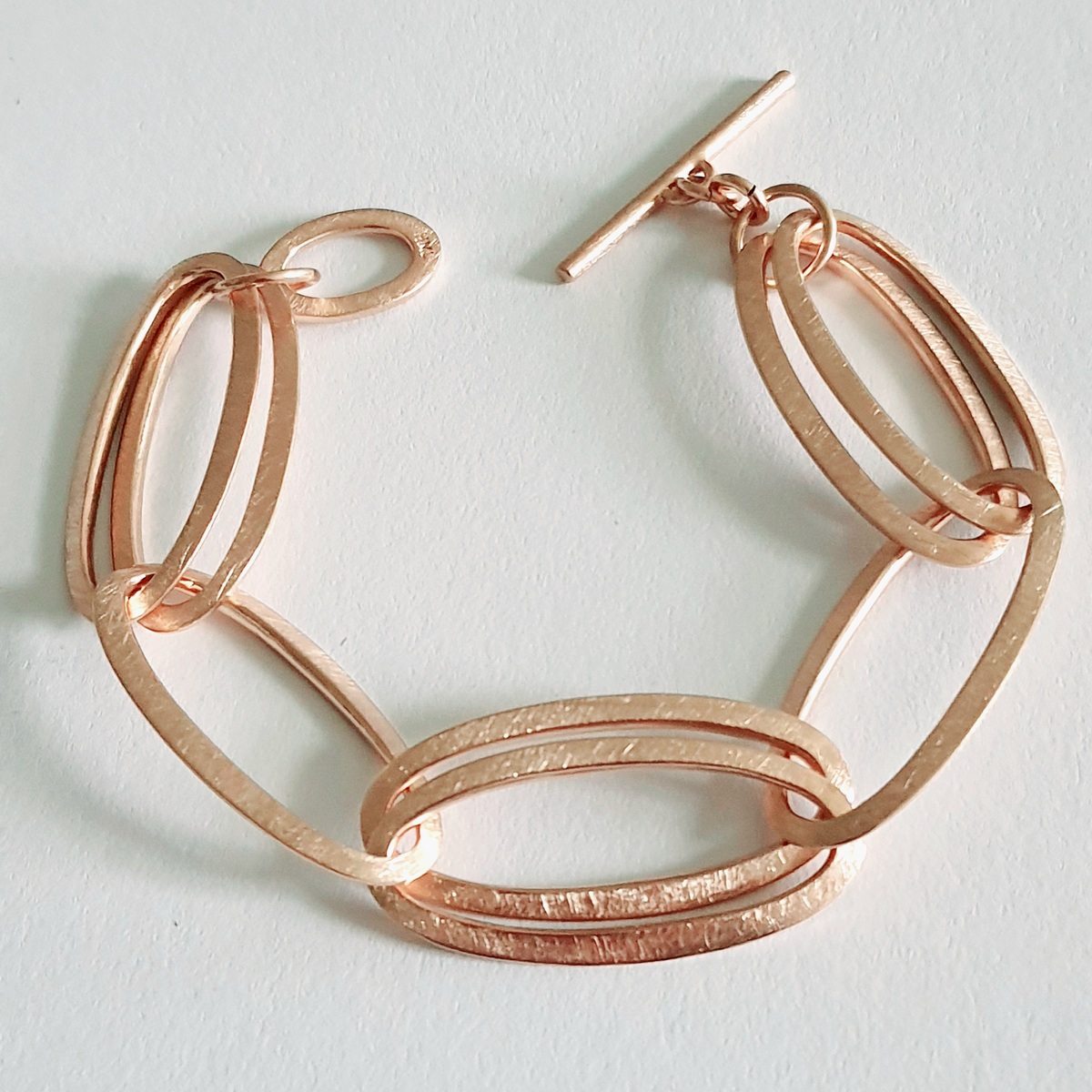 Ein elegantes Armband aus Roségold mit mehreren ovalen Gliedern und einem T-Verschluss. Das Design ist stilvoll und luxuriös.
