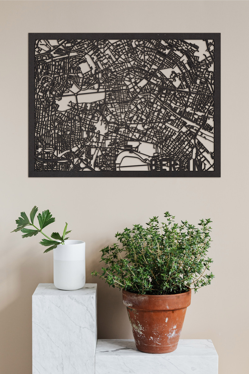 Ein kunstvoller und detaillierter Holzschnitt der Stadtkarte von Berlin, stilvoll an einer beigefarbenen Wand hängend. Darunter stehen dekorative Pflanzen auf Marmorblöcken.