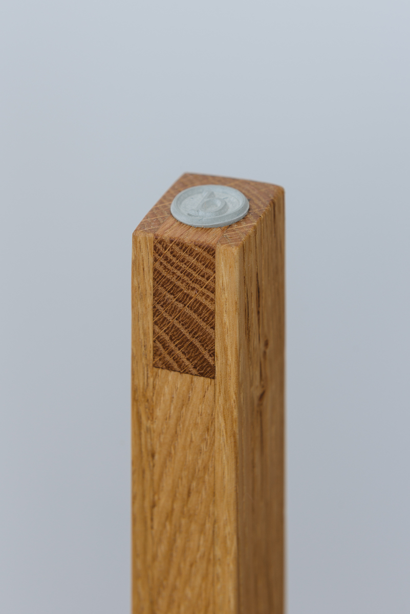 Nahaufnahme eines Stehpults aus Holz mit einer metallischen Münze oben aufgesetzt. Das Design ist minimalistisch und die Oberfläche aus natürlichem Holz wirkt elegant.