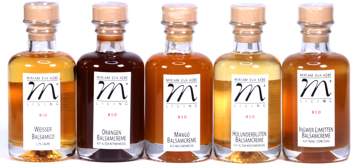 Das Bild zeigt ein Essig-Set »Hell« mit fünf verschiedenen Sorten Balsamico: Weißer Balsamico, Orangen Balsamico, Mango Balsamico, Holunderblüten Balsamico und Ingwer Limetten Balsamico. Jede Flasche hat ein Etikett und einen Holzverschluss.